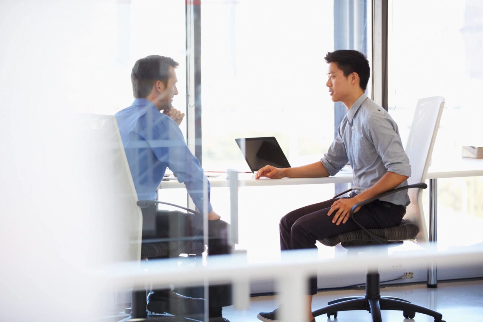 Two men sitting at a table with laptops.