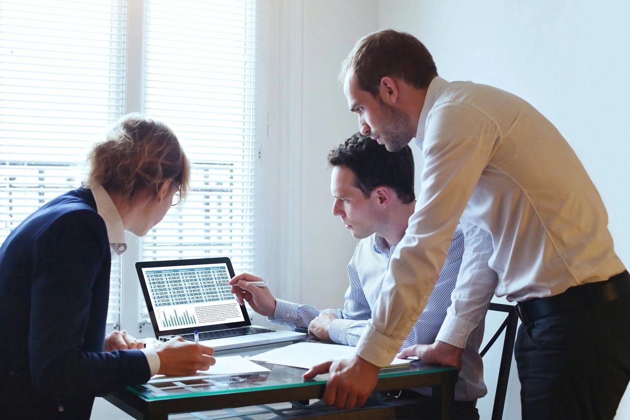 Three men are looking at a laptop screen.